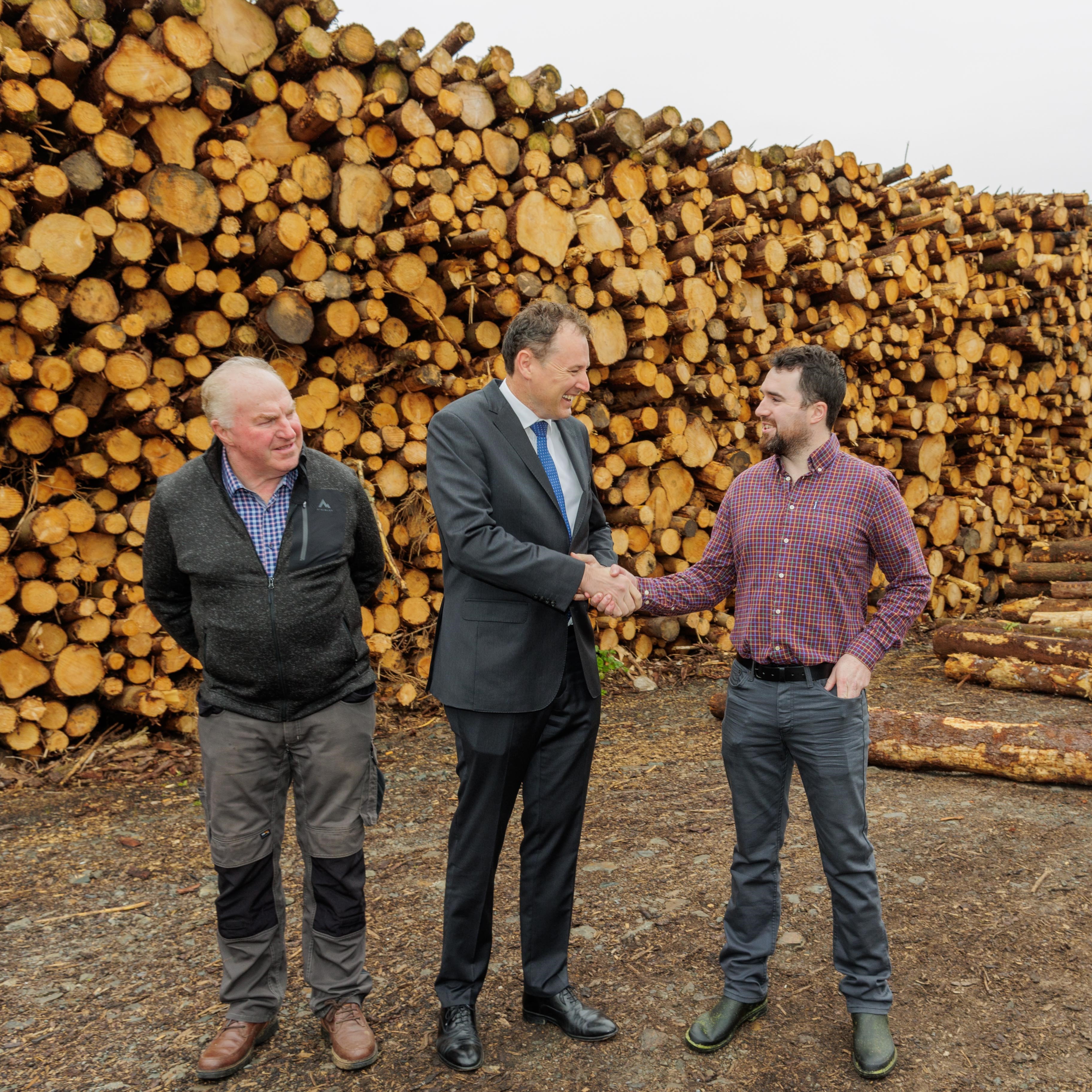 Kenny McCauley with visitors beside timber stacks at McCauley Wood Fuels